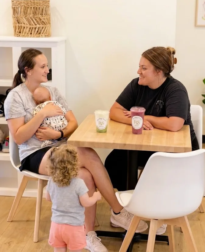 Moms relaxing with coffee and kids at a café table in The Play Social